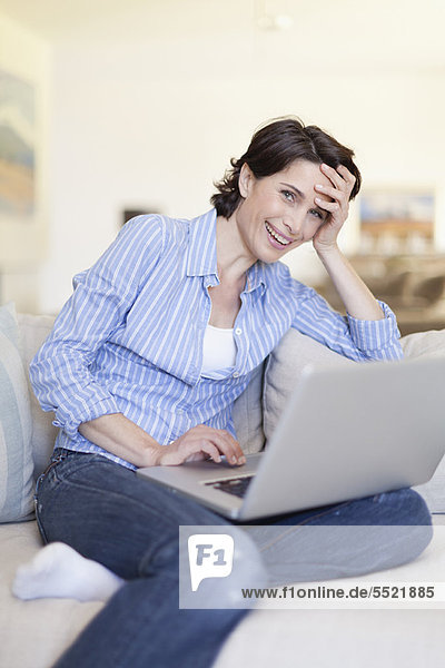 Lächelnde Frau mit Laptop auf der Couch