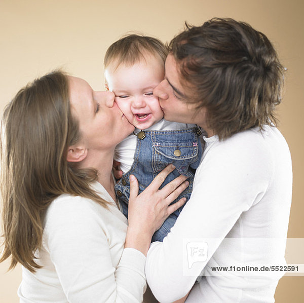 Eltern küssen lächelndes Kleinkind