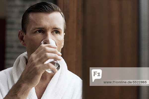 Man in bathrobe drinking water by window