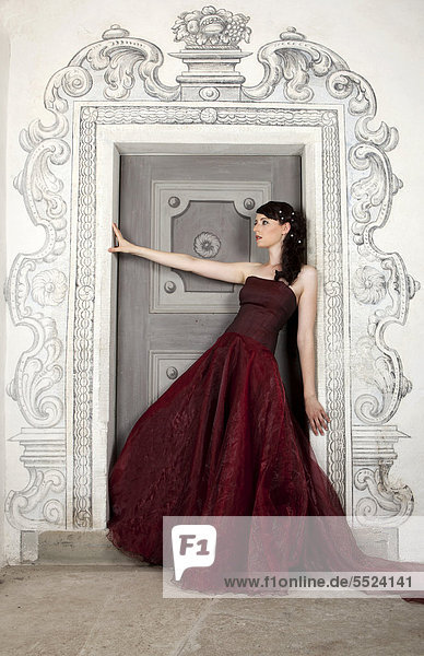 Junge Frau mit rotem Kleid und langer Schleppe steht an Tür