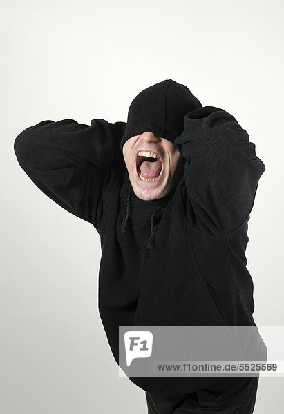 Young man wearing a black hooded shirt with his eyes under the hood  screaming madly and desperately
