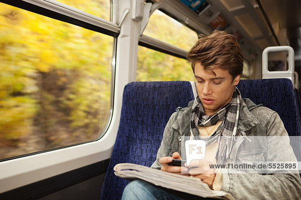 Junger Mann  der mit dem Handy im Zug unterwegs ist.