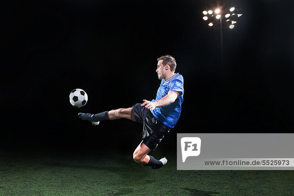 Junger Fußballspieler springt in die Luft  um den Ball zu kicken.