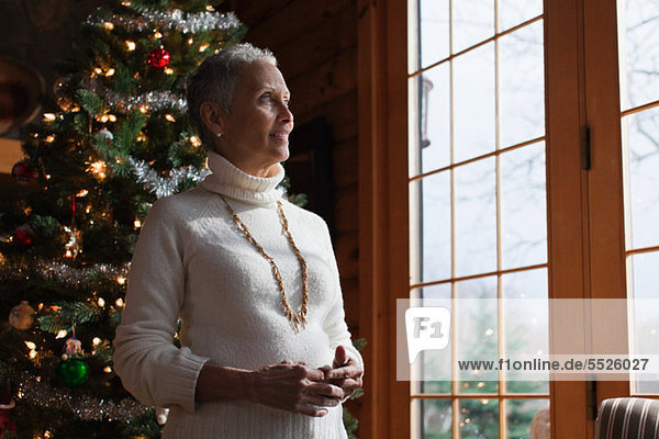Mature woman standing by Christmas tree  looking through window