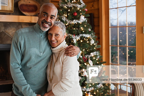 Mature couple embracing by Christmas tree  portrait