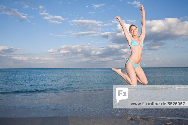 Mittlere erwachsene Frau im Bikini beim Springen am Strand