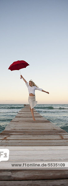 Junge Frau beim Springen auf dem Pier mit Regenschirm