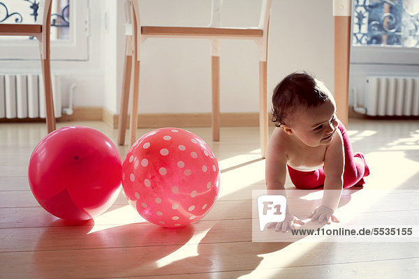 Kleinkind kriecht durch rosa Ballons