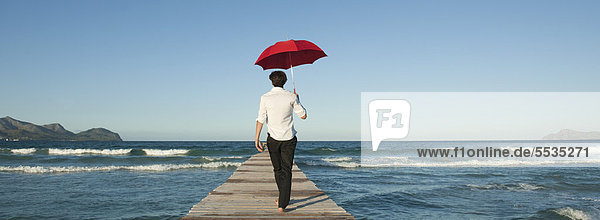Mann auf Pier mit Regenschirm  Rückansicht