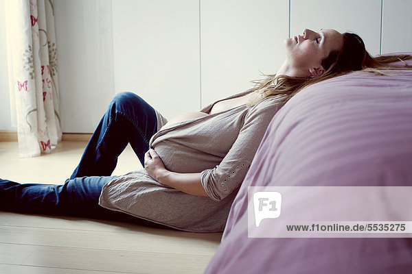 Schwangere Frau  die sich gegen das Bett lehnt.