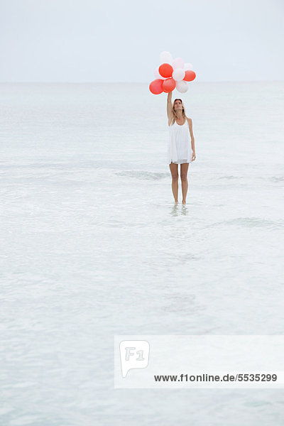 Woman standing on surface of water  holding bunch of balloons