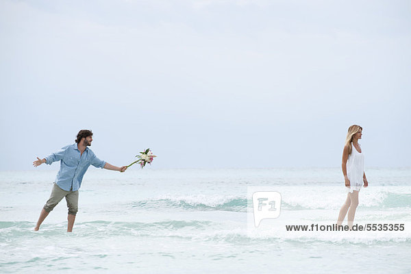 Couple standing in sea  woman walking away from man as he holds out a bouquet