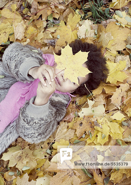 Kleines Mädchen auf Herbstlaubbett liegend