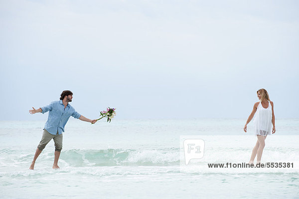 Couple walking apart in sea  man holding out bouquet