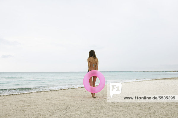 Frau steht am Strand  hält aufblasbaren Ring  Rückansicht