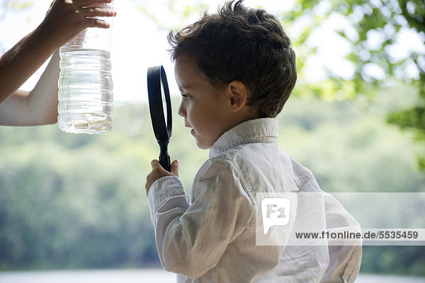 Junge studiert Fisch in Wasserflasche mit Lupe