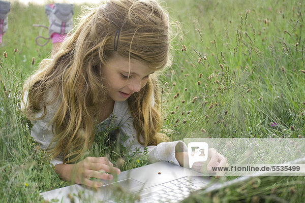 Mädchen im Gras liegend  Marienkäfer beim Krabbeln am Laptop beobachtend