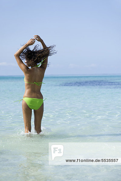 Frau im Bikini springend im Wasser mit fliegendem Haar
