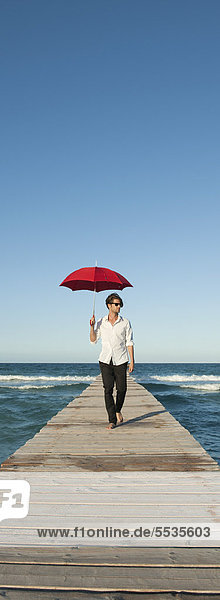 Junger Mann auf dem Pier mit Regenschirm