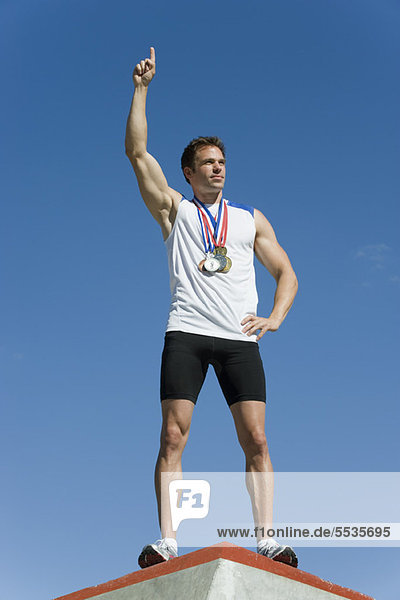 Männlicher Athlet auf dem Siegerpodest mit erhobener Hand im Sieg