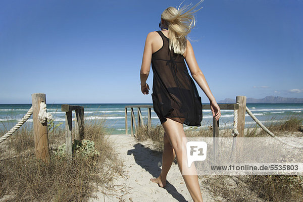 Woman walking on beach path toward sea  rear view