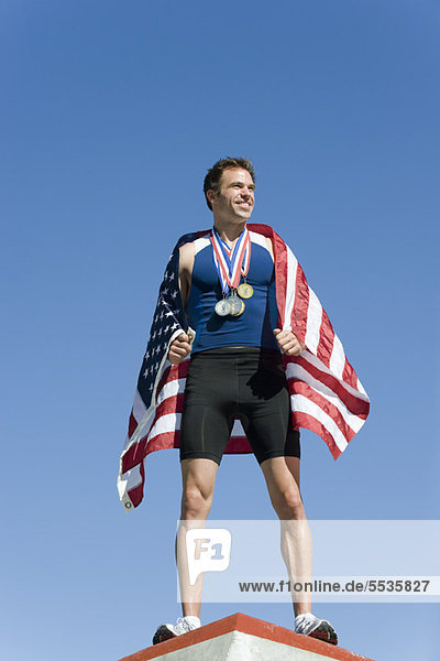 Männlicher Athlet auf dem Siegertreppchen  in amerikanische Flagge gehüllt