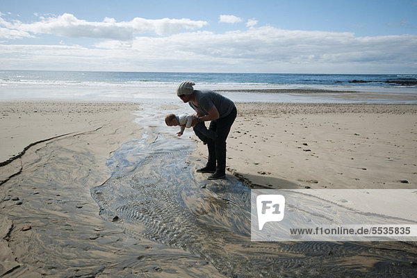 Vater und Kleinkind beim Blick auf den geriffelten Sand am Strand