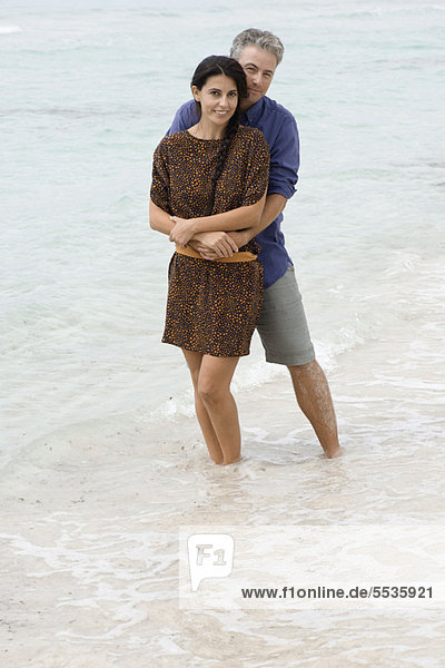 Mann und Frau umarmen sich am Strand  Knöchel tief im Wasser. Portrait