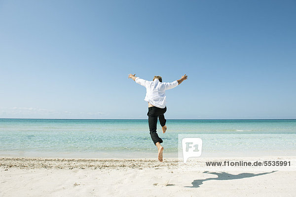 Man jumping midair on beach  rear view