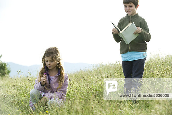 Children in field  boy reading book while girl picks wildflowers