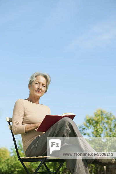 Seniorin im Freien sitzend mit Buch  Portrait