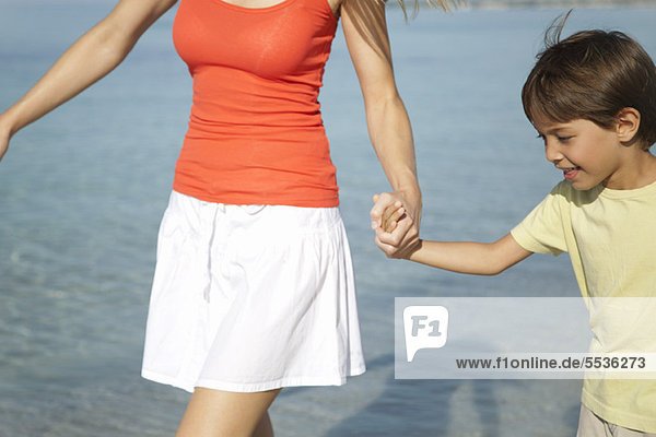 Boy holding his mother's hand at the beach