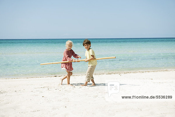 Boy and girl holding stick together on beach