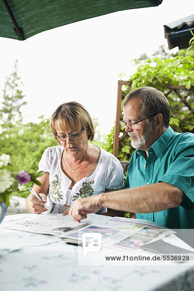 Senior couple sitting in back yard of house reading newspaper