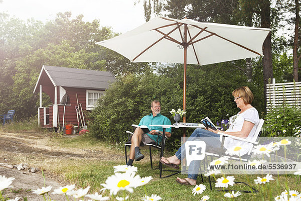 Seniorenpaar entspannt im Garten unter dem Sonnenschirm sitzend