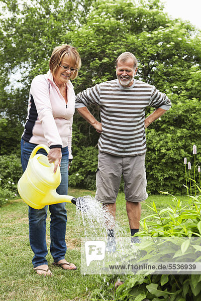 Senior woman watering to plants while husband with hands on hip watching
