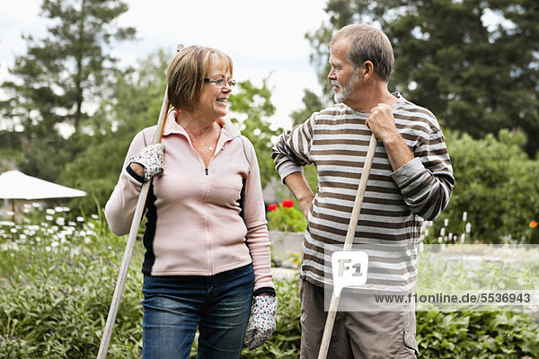 Front view of senior couple standing in back yard with rake