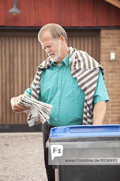 Älterer Mann  der Zeitung liest  steht in der Nähe des Mülleimers.