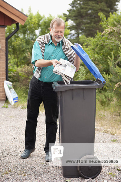 Älterer Mann wirft Zeitung in die Mülltonne