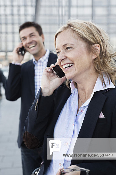 Glückliche Frau am Telefon mit Geschäftsmann im Hintergrund