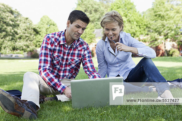 Geschäftsleute sitzen auf Rasen mit Laptop im Park
