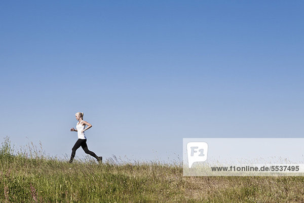 Full length of young woman jogging against blue sky