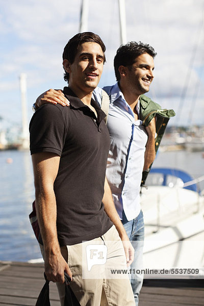 Junge männliche Freunde  die auf dem Pier mit dem Arm herumlaufen.