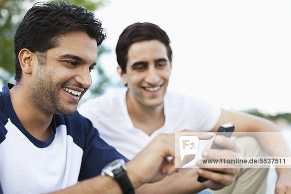 Close-up of young man using mobile phone while friend looking