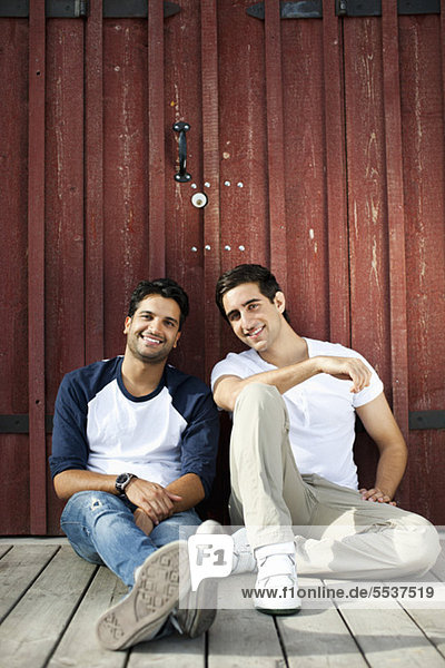 Porträt junger männlicher Freunde  die vor einer Holzwand sitzen