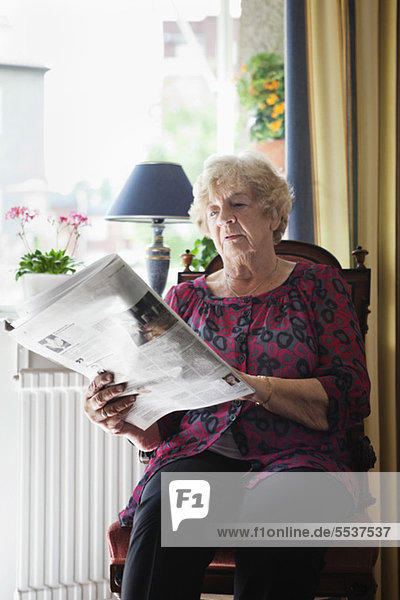 Entspannte Seniorin beim Zeitungslesen zu Hause
