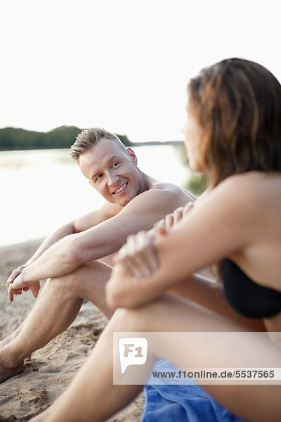 Mittlerer erwachsener Mann mit Frau auf Strandtuch sitzend