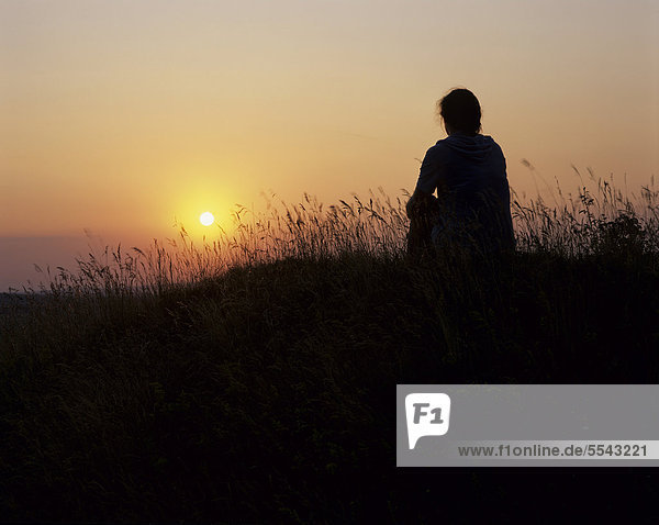 Silhouette einer jungen Frau die sitzend in den Sonnenuntergang schaut  Thüringen  Deutschland  Europa