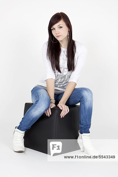 Young woman wearing a white top and jeans  posing on a black cube seat