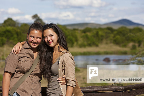 Two girls  about 13 and 18  wearing safari outfits leaning against on a railing  Masai Mara National Reserve  Kenya  East Africa  Africa  PublicGround